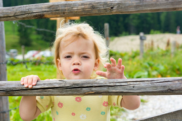 Cute blonde girl climbing across wooden fence on mountain pasture.