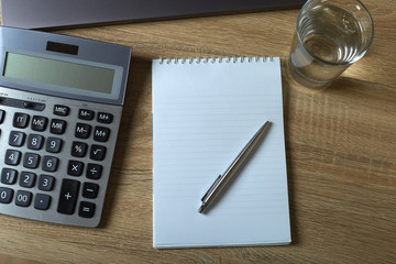 Remote work laptop calculator notepad with pen and glass of water on the table