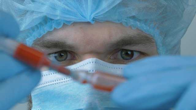 Man in protective gear taking samples for Coronavirus vaccine for 2019-nCoV COVID virus. Male scientist with syringe for injection. Young laborant takes blood samples for prevention of viral diseases