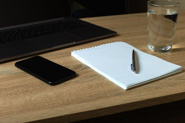 Remote work laptop notepad with pen and glass of water on the table