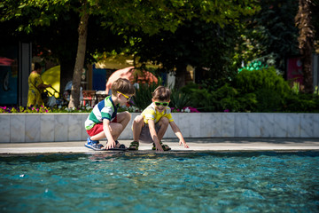 Group of happy children playing outdoors near pool or fountain. Kids having fun in park during summer vacation. Dressed in colorful t-shirts and shorts with sunglasses. Summer holiday concept