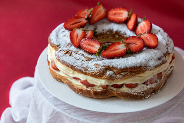 Delicious strawberries cream cake decorated with fresh cut strawberries on a white plate on the red background.