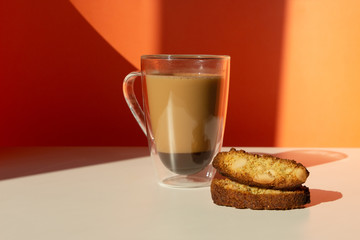 Biscotti almond cookies and a cup of coffee on the table on orange background. Geometric minimalist composition with shadow.