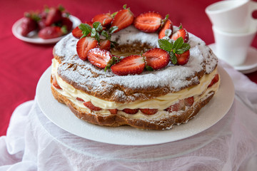 Delicious strawberries cream cake decorated with fresh cut strawberries on a white plate on the red background.