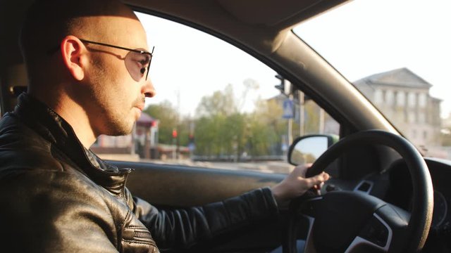 A man in a leather jacket and sunglasses riding in a car.