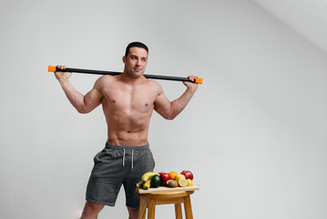A young sexy athlete stands with a bodybar on a white background.