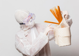 female in protection suit and glasses with mask holds toilet paper and pasta