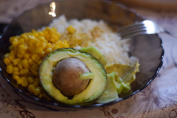Healthy food consisting of avocado, rice and corn in a plate in the kitchen