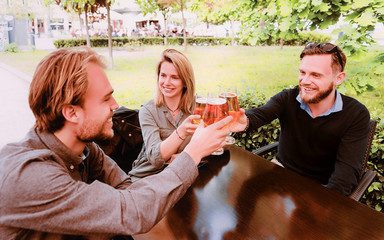 Smiling young friends clanging glasses of beer