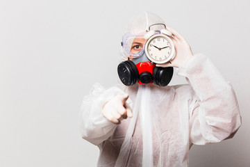 female doctor in protection suit and glasses with mask holds alarm clock
