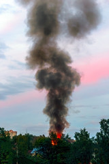 the building burns with fire and black smoke against the evening sky