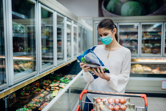 Woman with hygienic mask shopping for supplies.CPandemic quarantine preparation.hoosing nonperishable food essentials from store shelves.Budget buying at a supply store.Food supplies shortage.