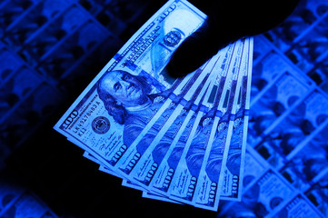 Counterfeit money checking with ultraviolet lamp. Fraud crime. Dollars inflation. Economic crisis.