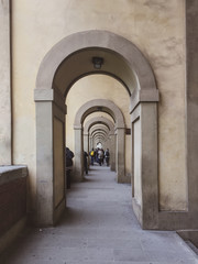 Fototapeta na wymiar a sidewalk full of architectural arches with people walking on the distance