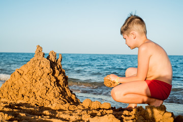 Sand castle made of sand by the hands of a child on the shore.Sea at sunset, white sand on the beach.Sunset sun, yellow light