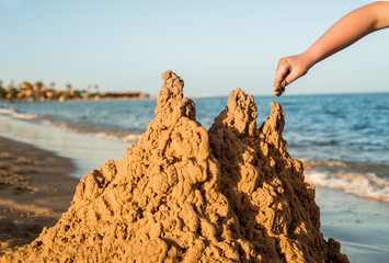 Sand castle made of sand by the hands of a child on the shore.Sea at sunset, white sand on the beach.Sunset sun, yellow light