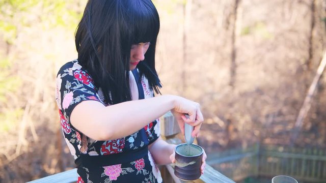 Closeup of young happy woman with black asian hair brewing, drinking and enjoying in hot water teacup cup Japanese matcha green tea outdoors outside in home backyard garden deck