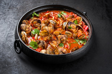 Cooked Japanese carpet shell with paprika and herbs in spicy tomato garlic sauce as closeup in a modern design pot
