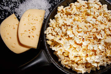Appetizing salted popcorn with cheese. Heap of homemade delicious popcorn on a rustic wooden table. Snacks and food for a movie theater or cinema. Fastfood background. Frying pan with corn and oil. .