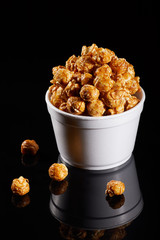 Appetizing caramel popcorn in the paper cup. Heap of homemade delicious popcorn on a wooden background. Snacks and food for a movie theater or cinema. Fastfood background.