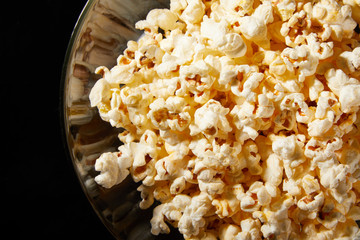 Glass bowl with salted popcorn with cheese. Heap of homemade delicious popcorn on a rustic wooden table. Snacks and food for a movie theater or cinema. Fastfood background. TV remote control