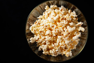 Glass bowl with salted popcorn with cheese. Heap of homemade delicious popcorn on a rustic wooden table. Snacks and food for a movie theater or cinema. Fastfood background. TV remote control
