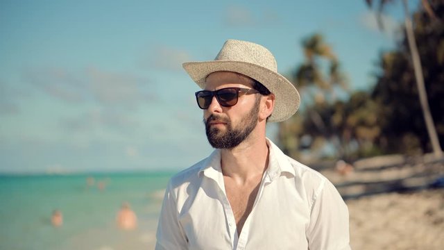  Guy In Sunglasses Walking On Tropical Beach.Guy Relaxing On Caribbean Beach.Beautiful Tanned Man In Hat Healthy Skin Sunbathing Enjoy Ocean Vacation.Happy Businessman Enjoying Tropical Beach Resort