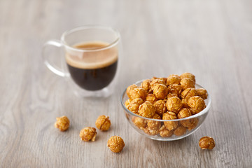 Appetizing caramelized popcorn and cup of coffee. Heap of homemade delicious popcorn on a wooden background. Snacks and food for a movie theater or cinema. Fastfood background.