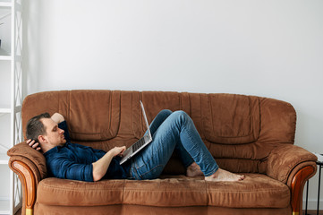 A man is lying at home on the sofa with a laptop