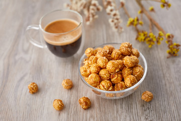 Appetizing caramelized popcorn and cup of coffee. Heap of homemade delicious popcorn on a wooden background. Snacks and food for a movie theater or cinema. Fastfood background.