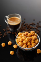Appetizing caramelized popcorn and cup of coffee. Heap of homemade delicious popcorn on a black mirror background. Snacks and food for a movie theater or cinema. Fastfood background.