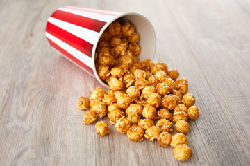 Appetizing caramel popcorn in the paper cup. Heap of homemade delicious popcorn on a wooden background. Snacks and food for a movie theater or cinema. Fastfood background.