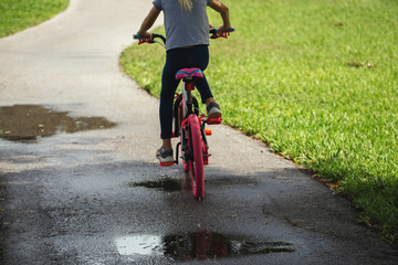 Child girl riding a bike in Park in the nature. Back view. Cyclist in summer park. Copy Space