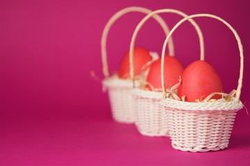 Fototapeta na wymiar Pink chicken eggs in a white wicker basket covered with straw a bright pink background. Holiday card with space for text.Easter symbol.Copy space.