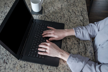 young professional woman sitting at her kitchen counter top working on her laptop computer
