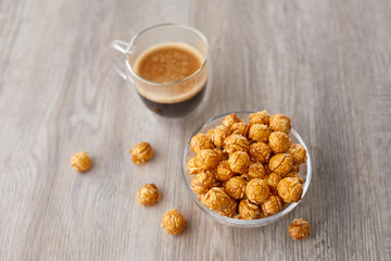 Appetizing caramelized popcorn and cup of coffee. Heap of homemade delicious popcorn on a wooden background. Snacks and food for a movie theater or cinema. Fastfood background.