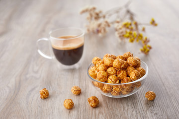 Appetizing caramelized popcorn and cup of coffee. Heap of homemade delicious popcorn on a wooden background. Snacks and food for a movie theater or cinema. Fastfood background.