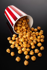 Appetizing caramel popcorn in the paper cup. Heap of homemade delicious popcorn on a black mirror background. Snacks and food for a movie theater or cinema. Fastfood background.