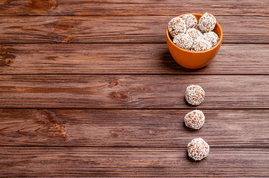Energy balls of dates, peanuts, oats, sprinkled with coconut in a clay brown cup on a wooden background with copy space with place for text.