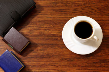 A cup of coffee and record book, note book on a wooden background.