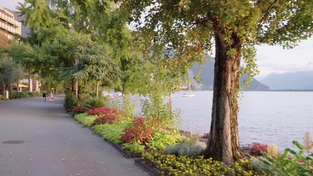 Flow shot magic hour time fromt Swiss promenade to Lake Geneva at Montreux through trees. Unrecognized tourists making photos