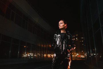 Naklejka premium Portrait of a girl on the street of a night city in leather clothes in the light of lanterns