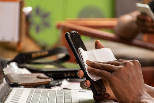 Black Man Cleaning The Surface Of His Mobile Phone With A Tissue