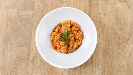creamy chicken fusilli pasta recipe with basil leaves and Parmesan cheese in a white plate on a wooden background