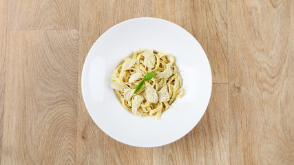 alfredo pasta with basil leaves and Parmesan cheese in a white plate on a wooden background