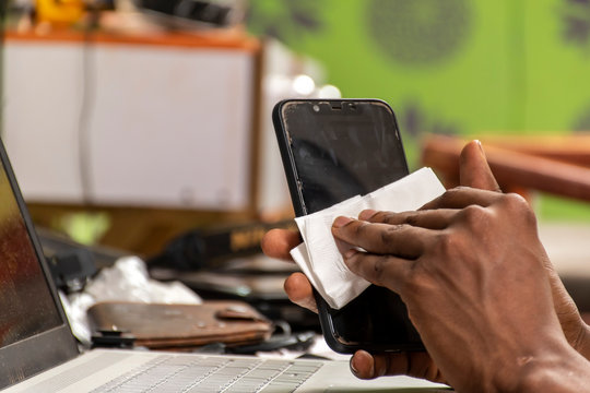 black man cleaning the surface of his mobile phone with a tissue