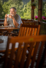 Handsome senior man enjoying his morning coffee on a mountain hotel terrace, while on vacation