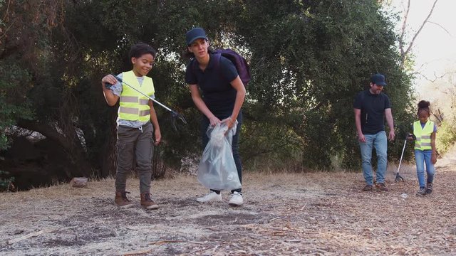 Adult team leaders with group of children at outdoor activity camp collecting litter together - shot in slow motion