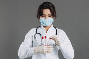 A female doctor in a mask holds test tubes, blood tests, potentially infected people with a...