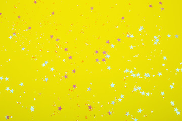Holographic stars and silver sparkles on bright yellow background. Festive backdrop for your projects.